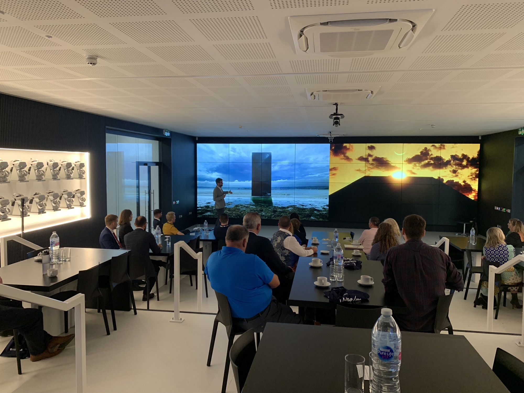 Corporate venue hire location - a large presentation space with audience sitting on chairs in front of two big screens.