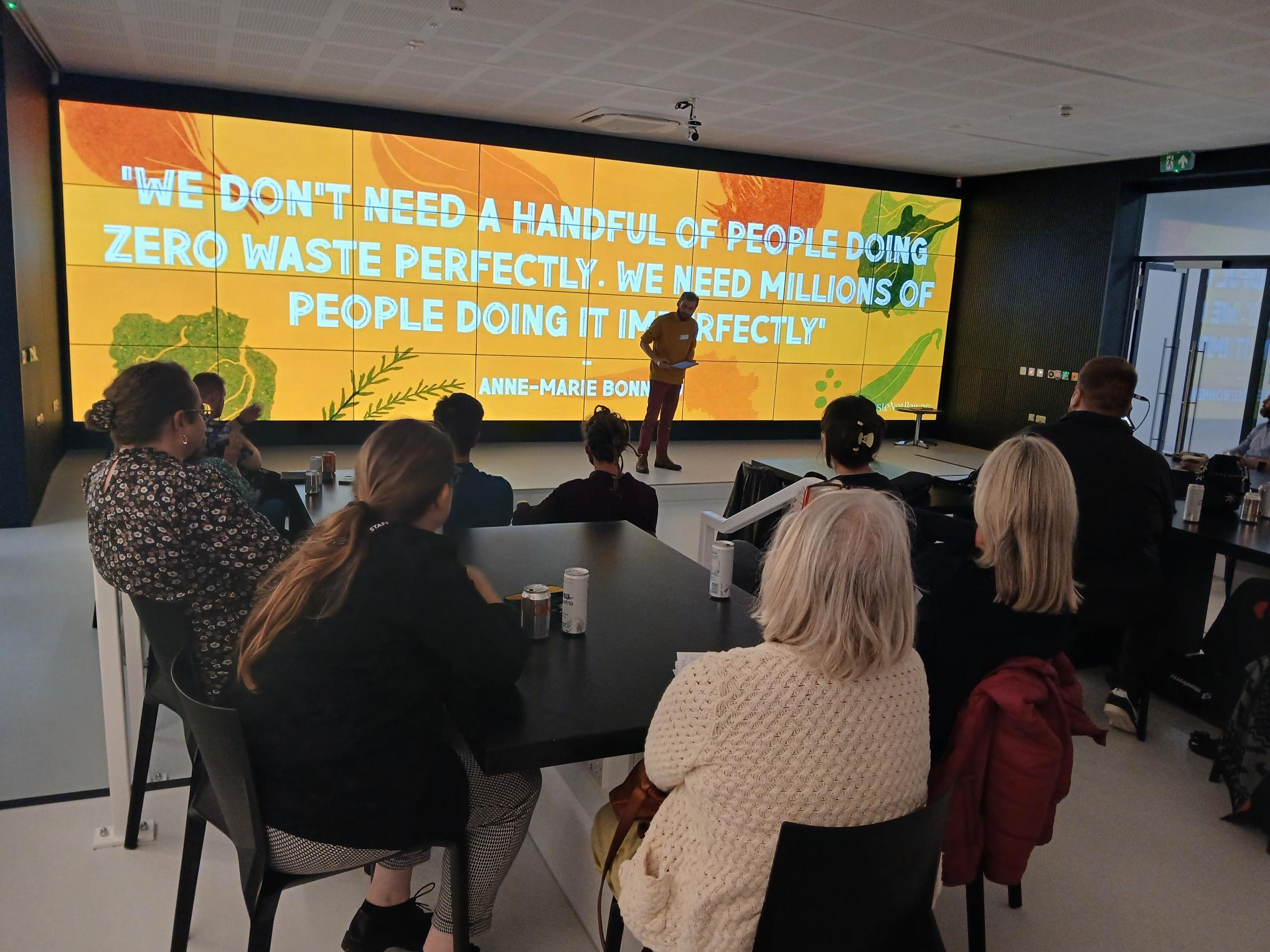 Someone conducting a talk on sustainability with people sat listening