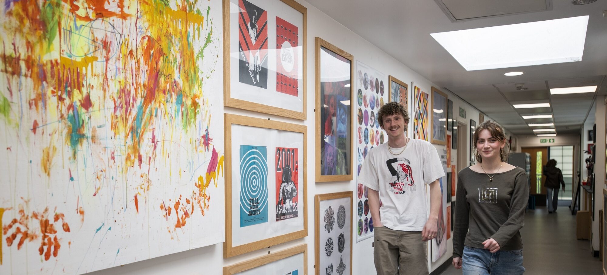 A boy and girl walking in a hallway with art on the wall at West Suffolk College Sixth Form's School of Art and Design.