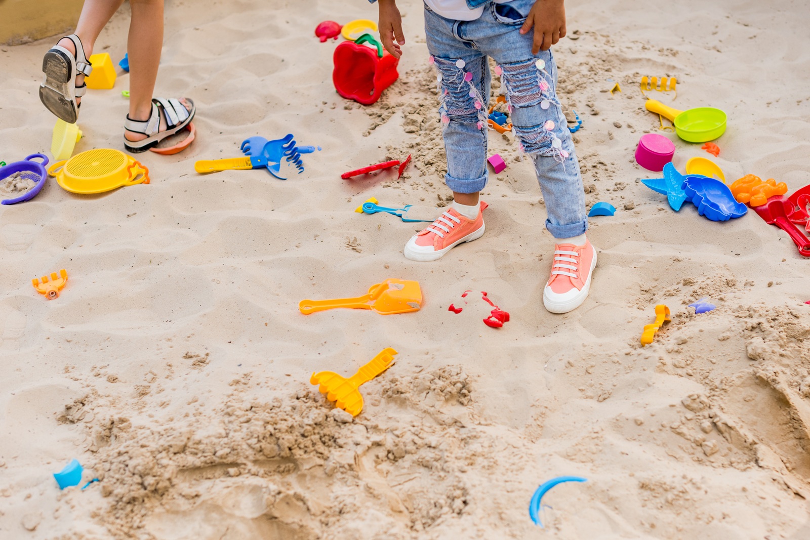 cropped image of two little girls in sandbox with plastic scoops, molds and bucket at playground